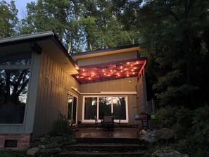 Une maison moderne dotée d’un patio couvert, d’un coin repas et offrant une vue sur les arbres environnants.