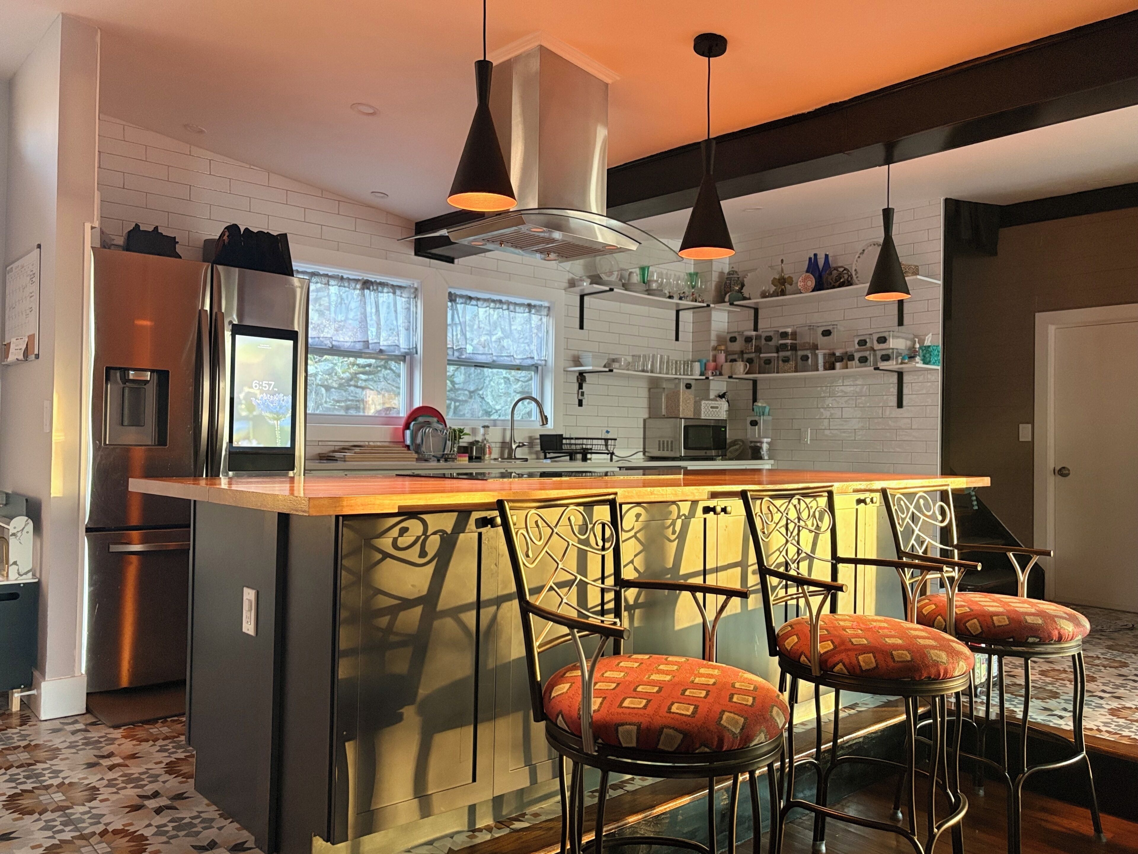 A kitchen with a central island, bar stools, a stainless steel refrigerator, and pendant lighting.