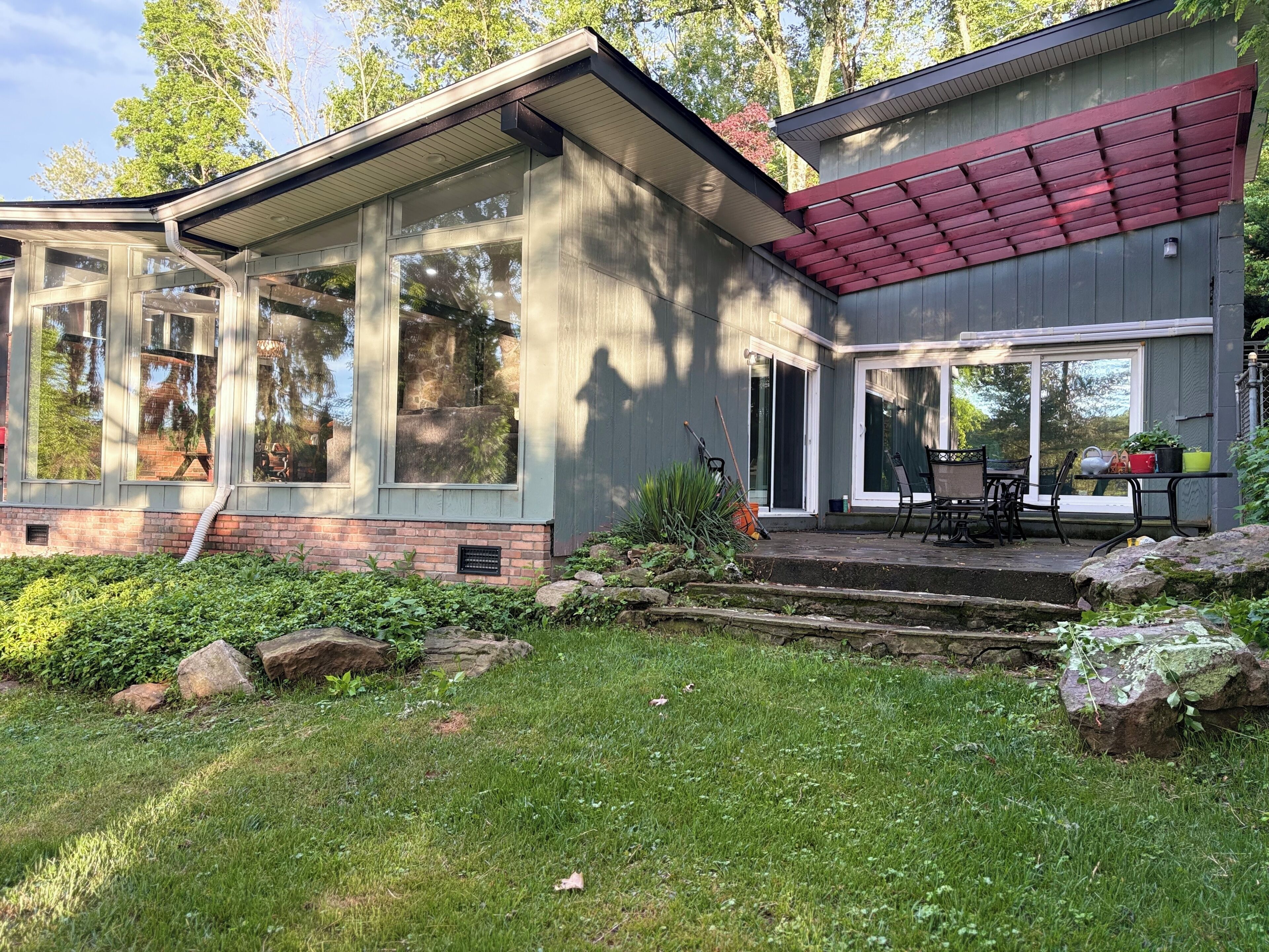 Une maison moderne dotée de grandes fenêtres, d’un patio couvert et d’un jardin bien entretenu.