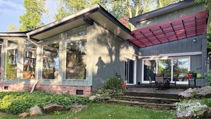 A modern house with large windows, a covered patio, and a well-maintained garden. - Spacious Lake Retreat, Stunning Sunset Views, Private Outdoor Entertaining. (Green Township)