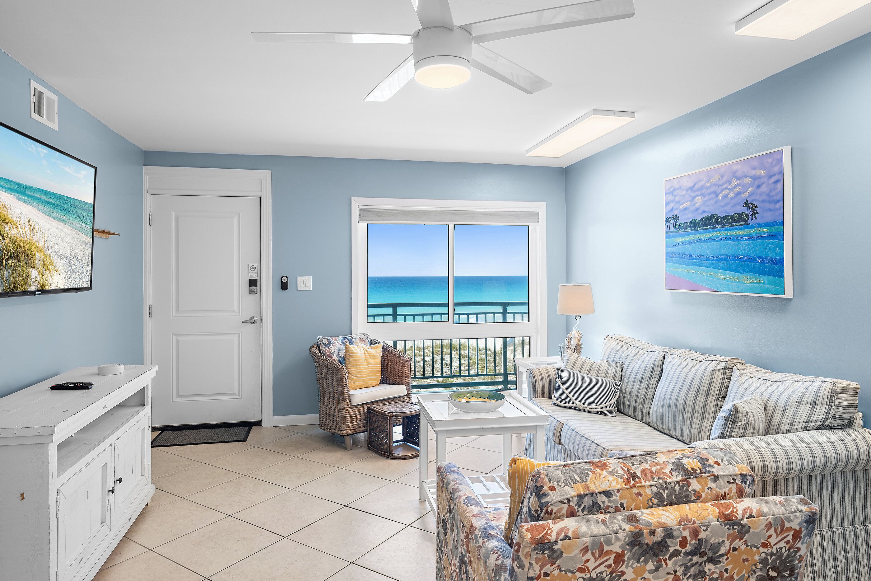 A living room with a view of the ocean, a ceiling fan, and a white door.