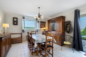 Un coin repas comprenant une table, des chaises, un lustre, une horloge et une vue par la fenêtre.