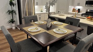 Una cucina moderna con mobili bianchi, elettrodomestici in acciaio inossidabile e zona pranzo con tavolo in legno scuro apparecchiato per quattro persone.
