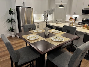 Eine moderne Küche mit weißen Schränken, Edelstahlgeräten und einem Essbereich mit einem dunklen Holztisch, gedeckt für vier Personen.