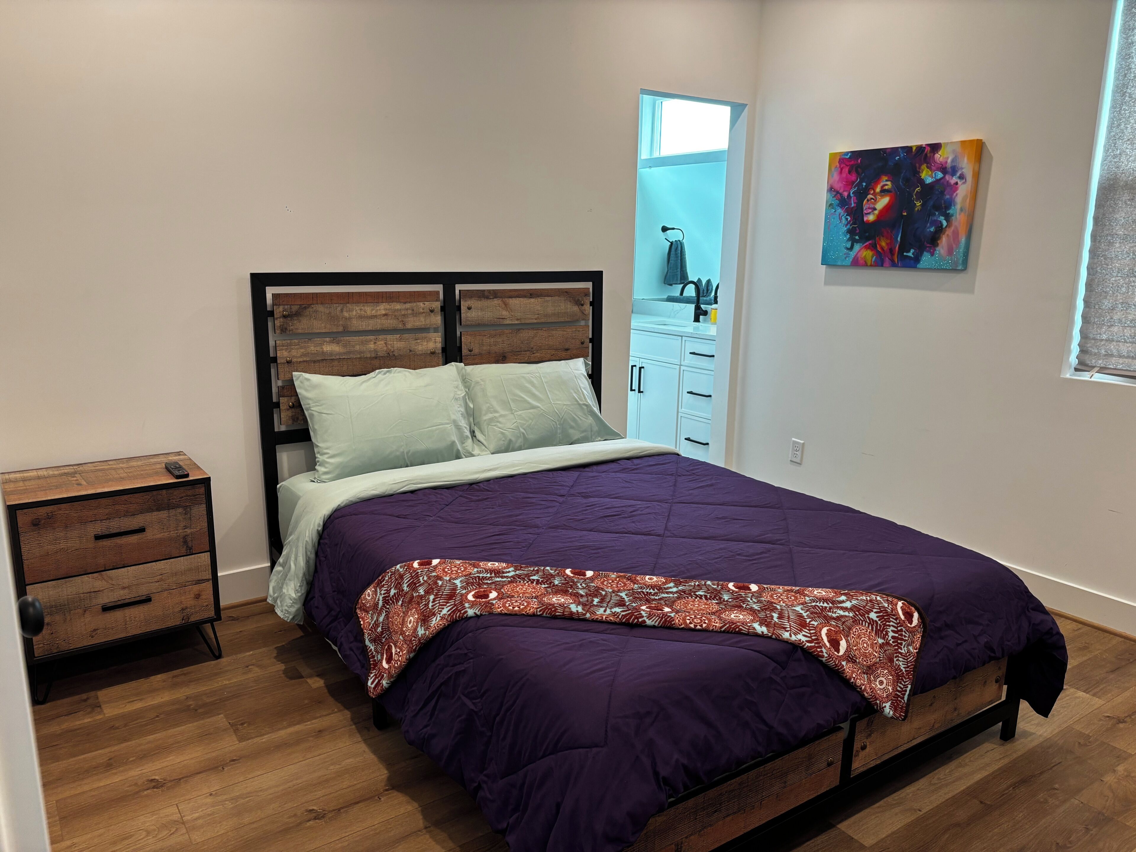 Una camera da letto con un letto, un comodino, una cassettiera, una finestra e un quadro.
