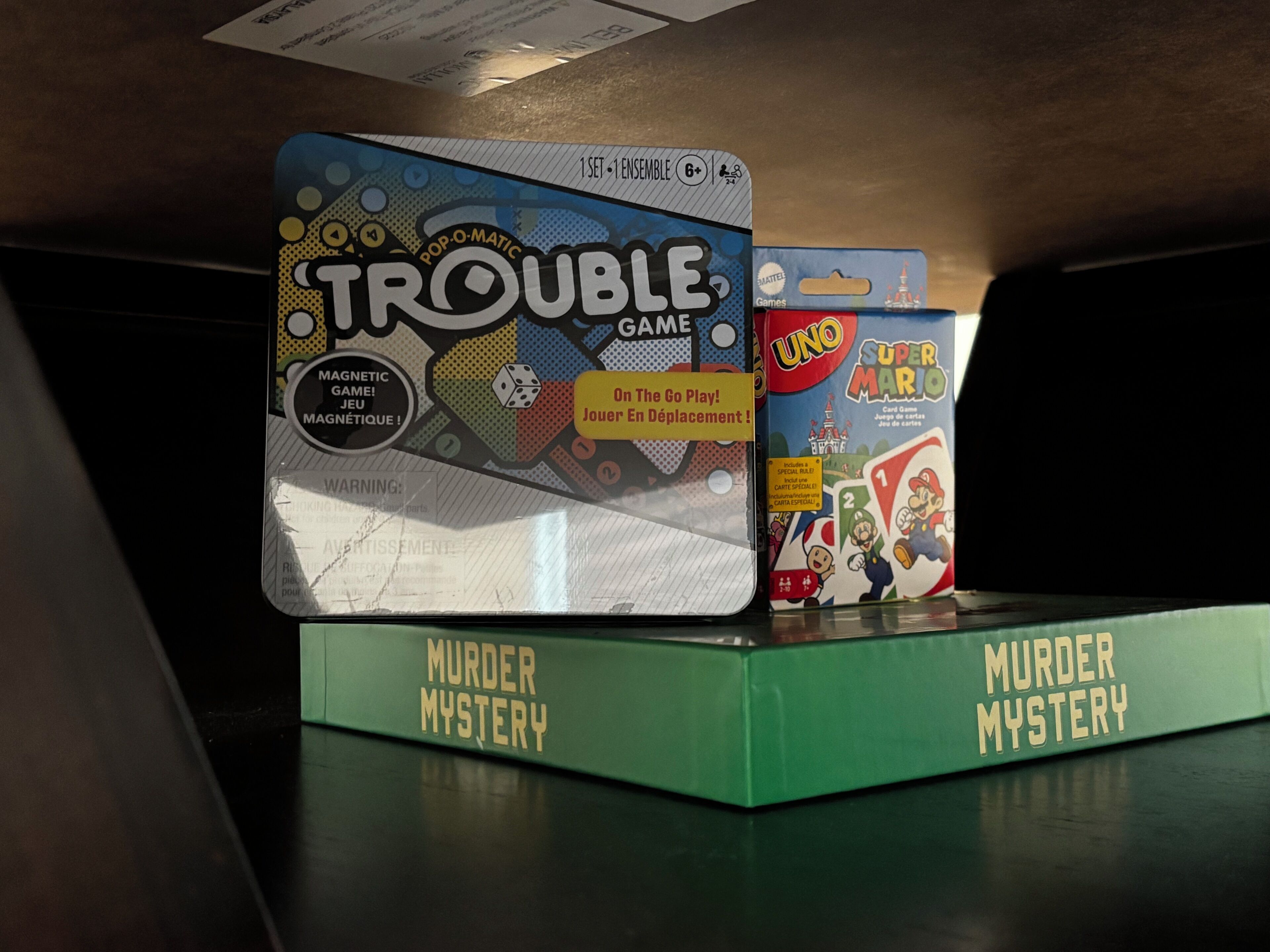 A game box labeled 'Trouble Game' and 'Murder Mystery' on a shelf.