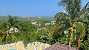 Zona de piscina con un porche cubierto, rodeada de palmeras y vistas al paisaje.