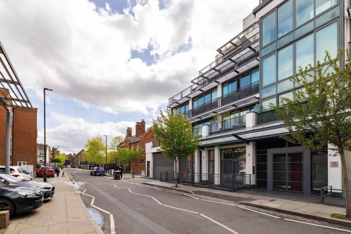A modern building with large windows and a flat roof, adjacent to a street with parked cars and a sidewalk.