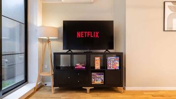 A room with a television on a stand, a lamp, and a window.