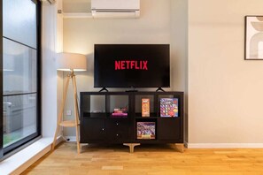 Ein Zimmer mit Fernseher auf einem Schrank, einer Lampe und einem Fenster.