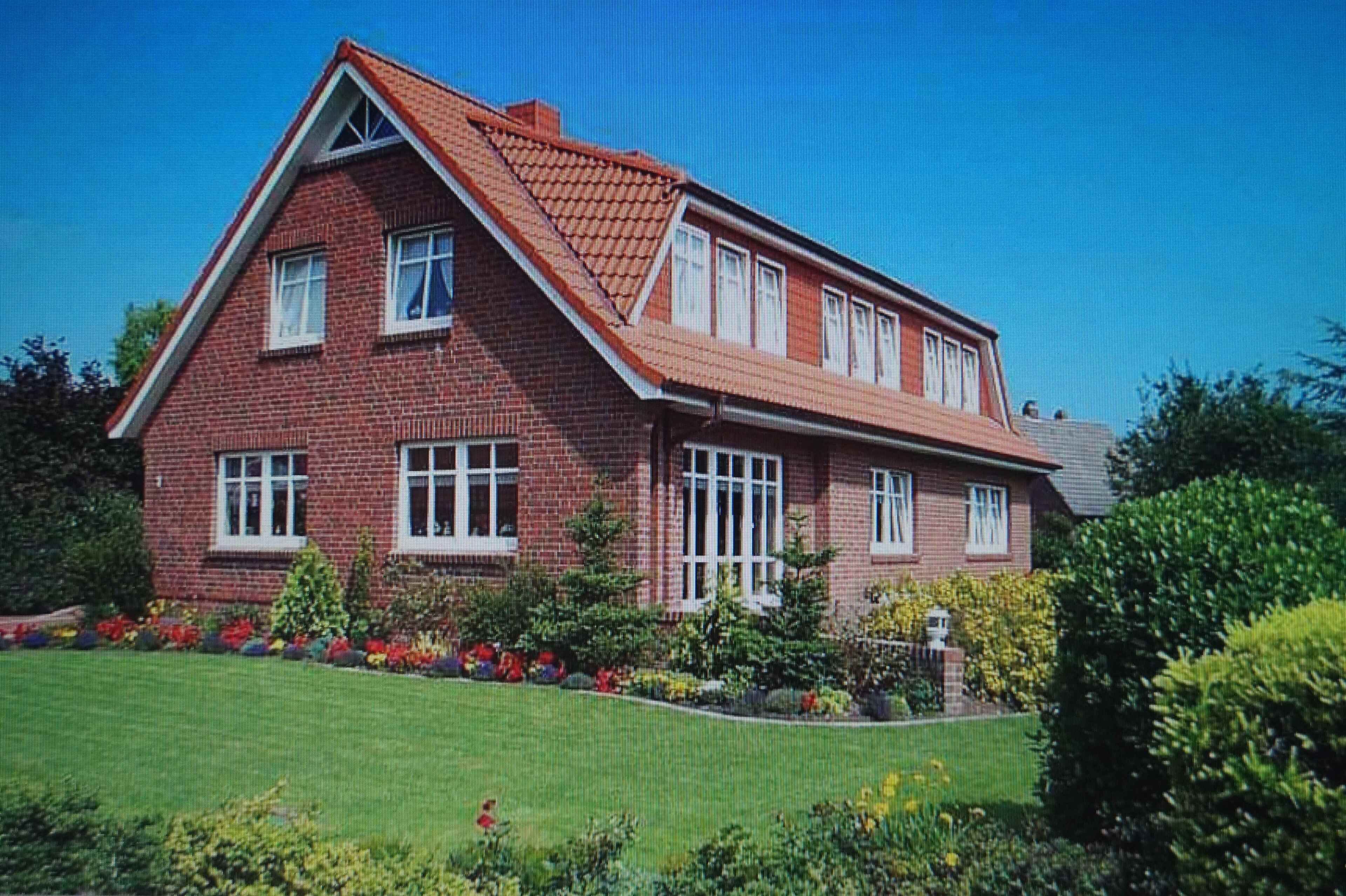 Een tweelaags bakstenen huis met schuin dak, veel ramen en een verzorgde tuin.