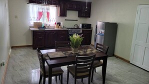 Una cocina compacta con armarios de madera oscura, una mesa de comedor con sillas, un ventilador de techo y un refrigerador.