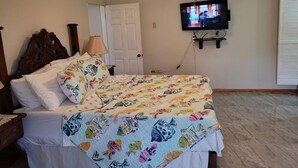 Un dormitorio con cama, ventilador de techo, televisor montado en la pared y una puerta.