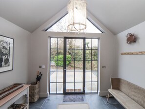 A modern interior with a large glass door leading to a garden, a wicker basket, a bench, and a framed picture on the wall. - Wood Meadow (Helston)