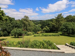 A well-maintained garden with a variety of trees and shrubs, a paved pathway, and a clear sky. - Wood Meadow (Helston)