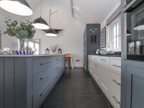 A modern kitchen with grey cabinetry, a central island, pendant lighting, and a view of the outdoors. - Wood Meadow (Helston)