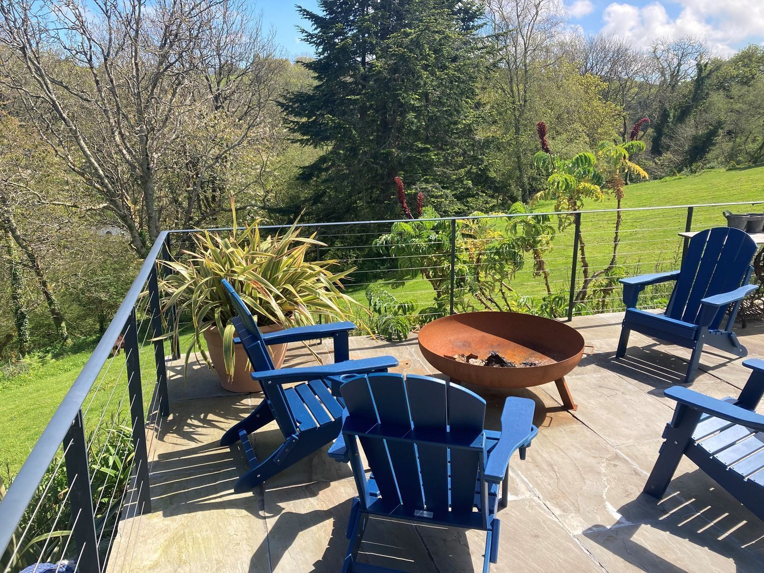 A patio with blue Adirondack chairs, a fire pit, and a potted plant.