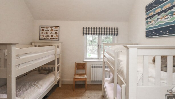 Ein Zimmer mit Etagenbetten, einem gerahmten Bild von Fischen, einem Fenster mit kariertem Vorhang und einem Gemälde.