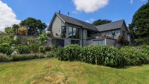 Ein modernes, zweistöckiges Haus mit einem großen Glasfenster, umgeben von einem gepflegten Garten und blauem Himmel.