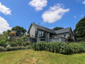 Ein modernes, zweistöckiges Haus mit einem großen Glasfenster, umgeben von einem gepflegten Garten und blauem Himmel.