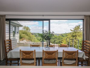 A dining area with a table, chairs, and a view of a landscape. - Wood Meadow (Helston)