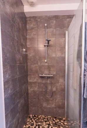 A shower with a glass door, a tiled floor, and a showerhead. - Château Besson (Désertines)