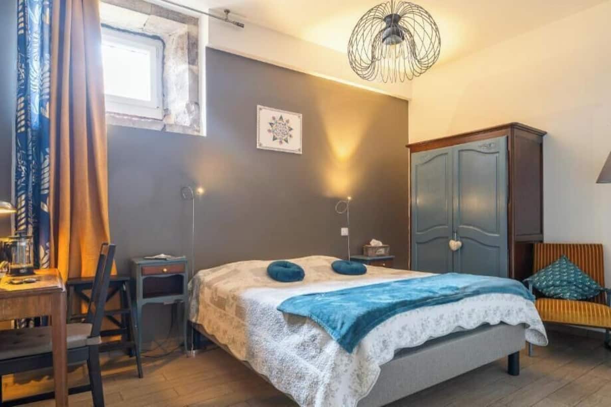 A bedroom with a bed, a desk, a chair, a wardrobe, and a lamp.