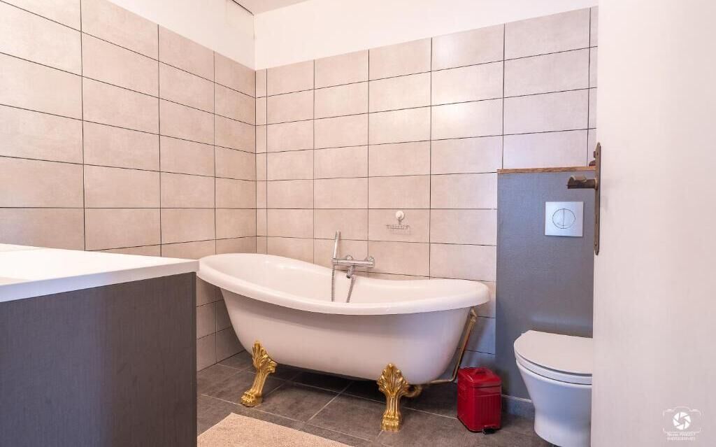 A bathroom with a freestanding bathtub, a toilet, and a red trash bin.