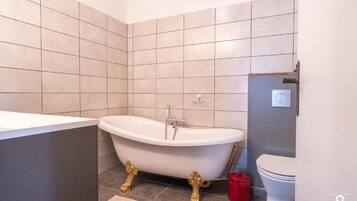 A bathroom with a freestanding bathtub, a toilet, and a red trash bin.