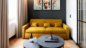 A living room with a mustard-colored sofa, two round tables, and three framed artworks on the wall. - Grodzka Apartments (Jelenia Góra)