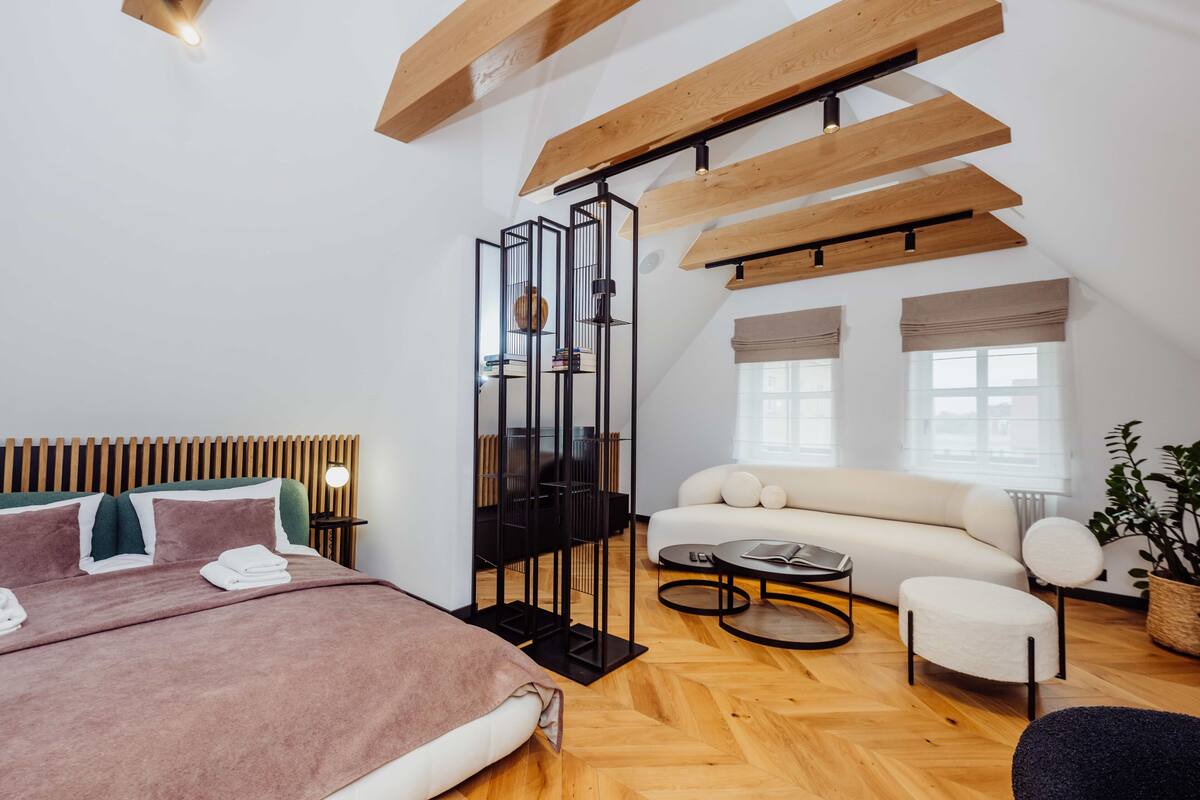 Ein modernes Hotelzimmer mit Holzboden, einem Bett mit Kopfteil, einer Couch, einem Couchtisch und einer Stehlampe.