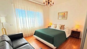 Quarto de hotel com cama, duas mesas de cabeceira, luminária, cadeira e um quadro na parede.
