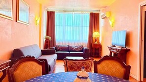 Quarto de hotel com mesa de jantar, sofá, televisão e cortinas.