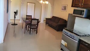 A kitchen with a stove, microwave, and dining area with chairs and a table. - Kingsbird By The Sea- Cozy 1 Bedroom (Runaway Bay)