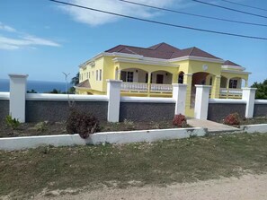 A two-story yellow house with a red roof, white columns, and a balcony. - Kingsbird By The Sea- Cozy 1 Bedroom (Runaway Bay)