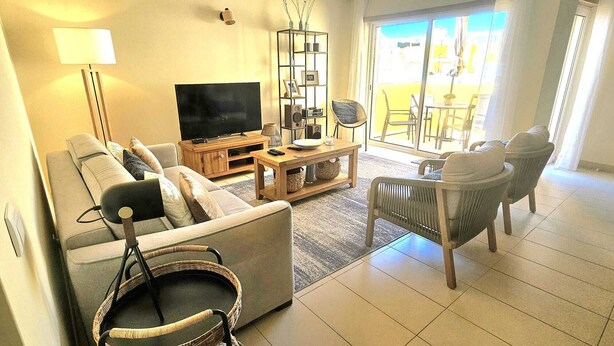 Una sala de estar con sofá, televisor, mesa de centro, sillón de mimbre y estantería.
