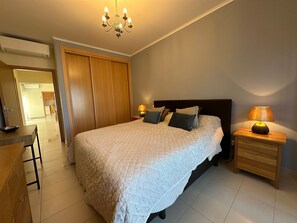 Une chambre à coucher comprenant un lit, des lampes de chevet, une armoire en bois, un bureau et une chaise.