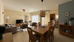 Una sala de estar con televisor, sofá y comedor con sillas y una mesa.