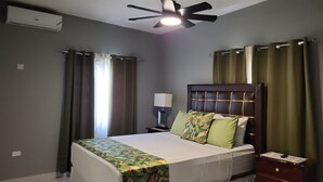 Ein Hotelzimmer mit einem Bett, einem Nachttisch, einer Lampe, einem Deckenventilator und Vorhängen.