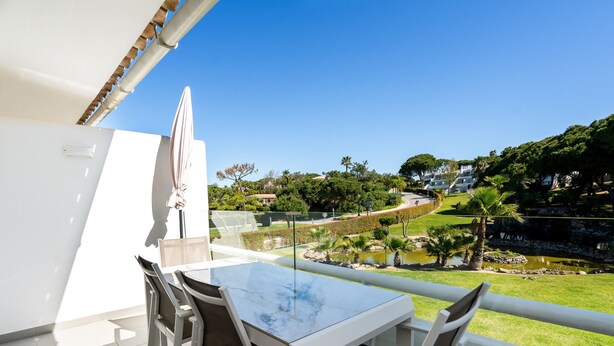 Ein Balkon mit Tisch und Stühlen, Blick auf einen angelegten Garten und einem strahlend blauen Himmel.