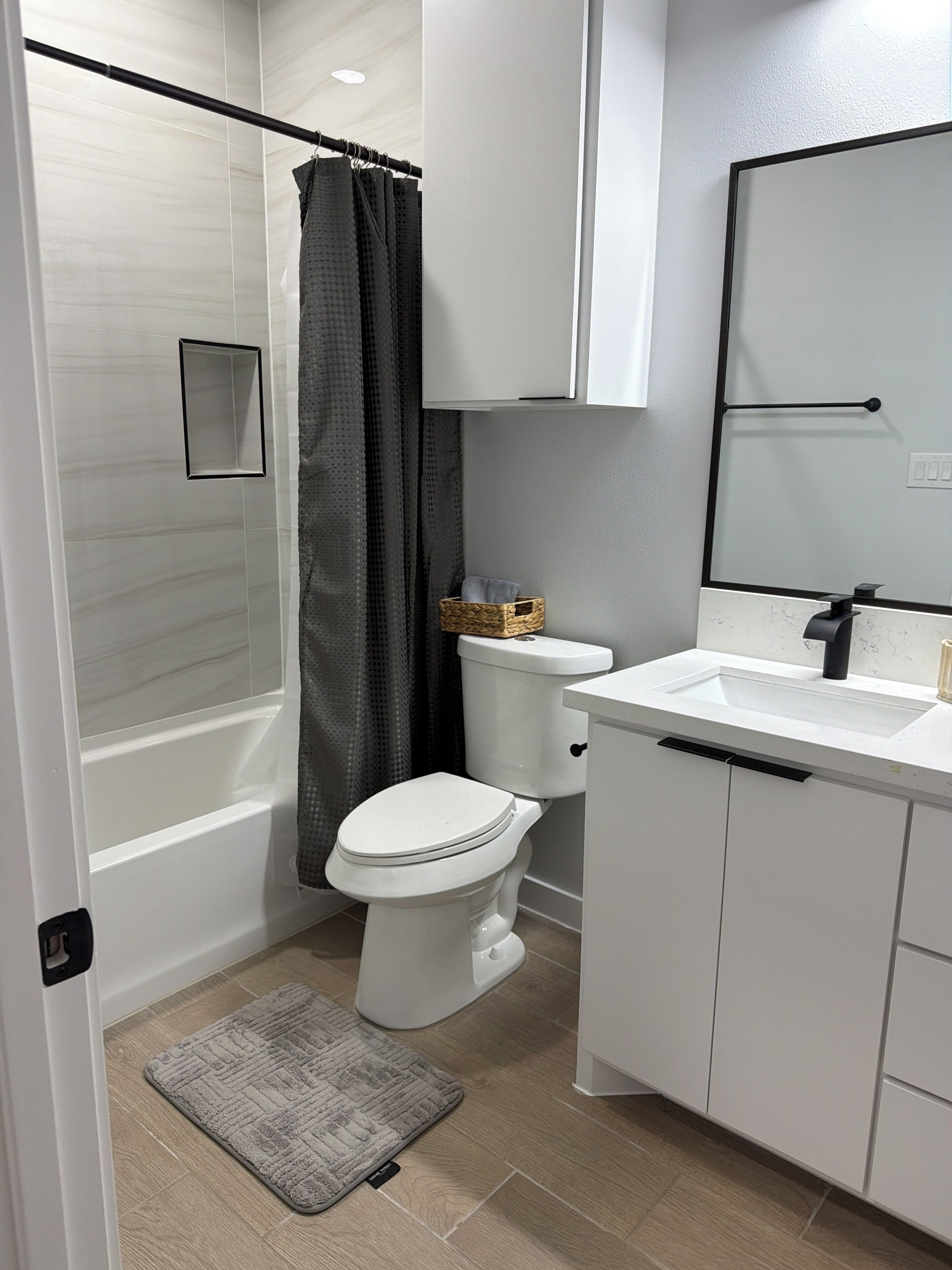 A bathroom with a shower, toilet, sink, and mirror.