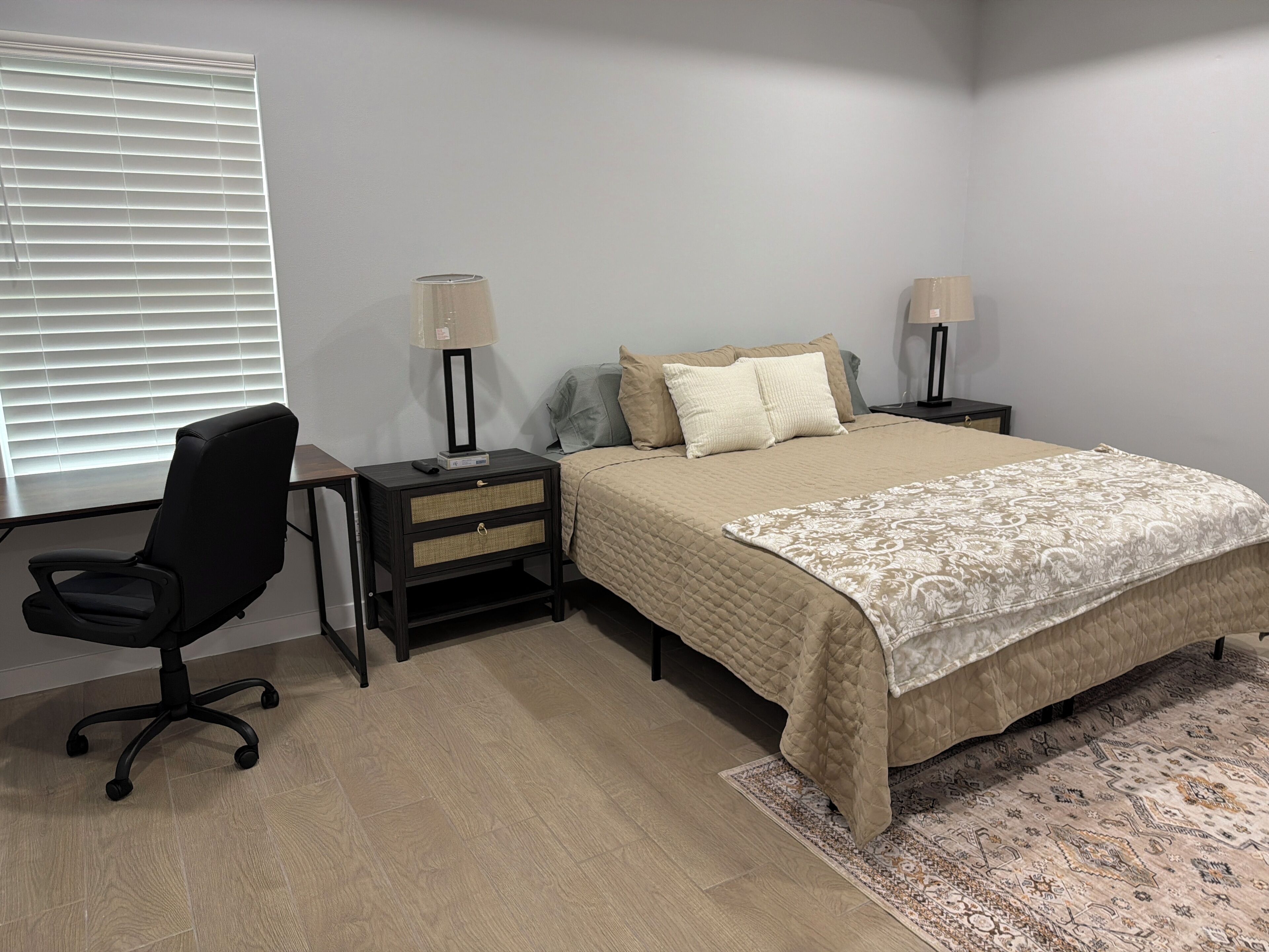 A bedroom with a bed, two bedside tables with lamps, a chair, and a window with blinds.