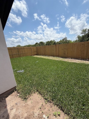 A fenced backyard with grass, a wooden fence, and a concrete wall. - 3BR Duplex 25 min to SpaceX, private Patio & Parking (Brownsville)
