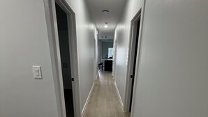 Un couloir aux murs blancs et au plancher en bois, qui mène à une cuisine.