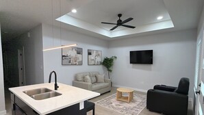 Une cuisine moderne dotée d’un îlot central, d’un coin repas avec un canapé et une table basse, d’un ventilateur de plafond et d’un téléviseur à écran plat fixé au mur.