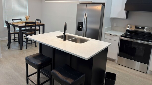 Une cuisine moderne dotée d’un îlot central, d’appareils électroménagers en acier inoxydable et d’un coin repas avec une table et des chaises.