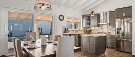 A modern kitchen with a central island, stainless steel appliances, and a dining area with a large window overlooking a pool.