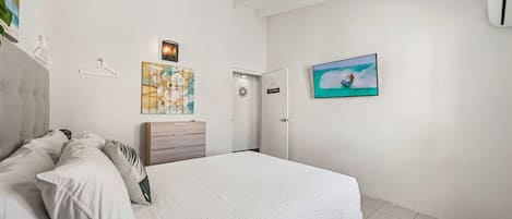 Een slaapkamer met een bed, een dressoir, een aan de muur bevestigde televisie en een deur.