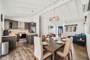 A spacious kitchen with modern appliances, a dining area with a wooden table and chairs, and a cozy living area with a blue sofa. - Exquisite Villa ~ 3 mins to beach w/ pool (Noord)