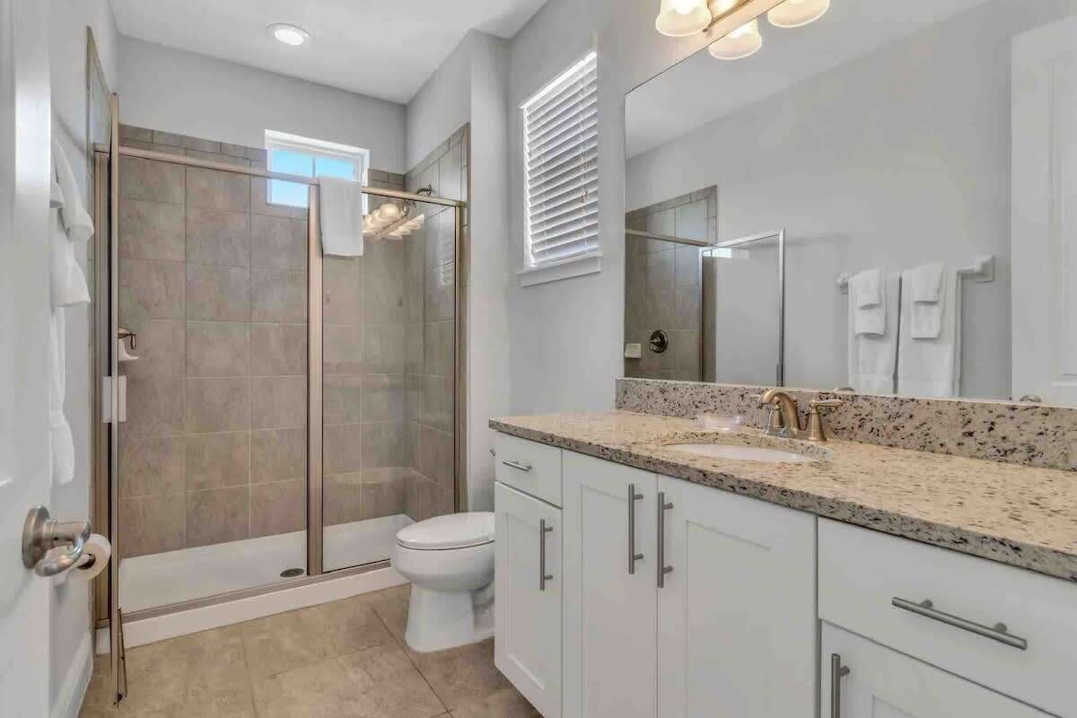Une salle de bain moderne avec une douche à parois de verre, des toilettes blanches et un lavabo sur un plan de travail en granit.